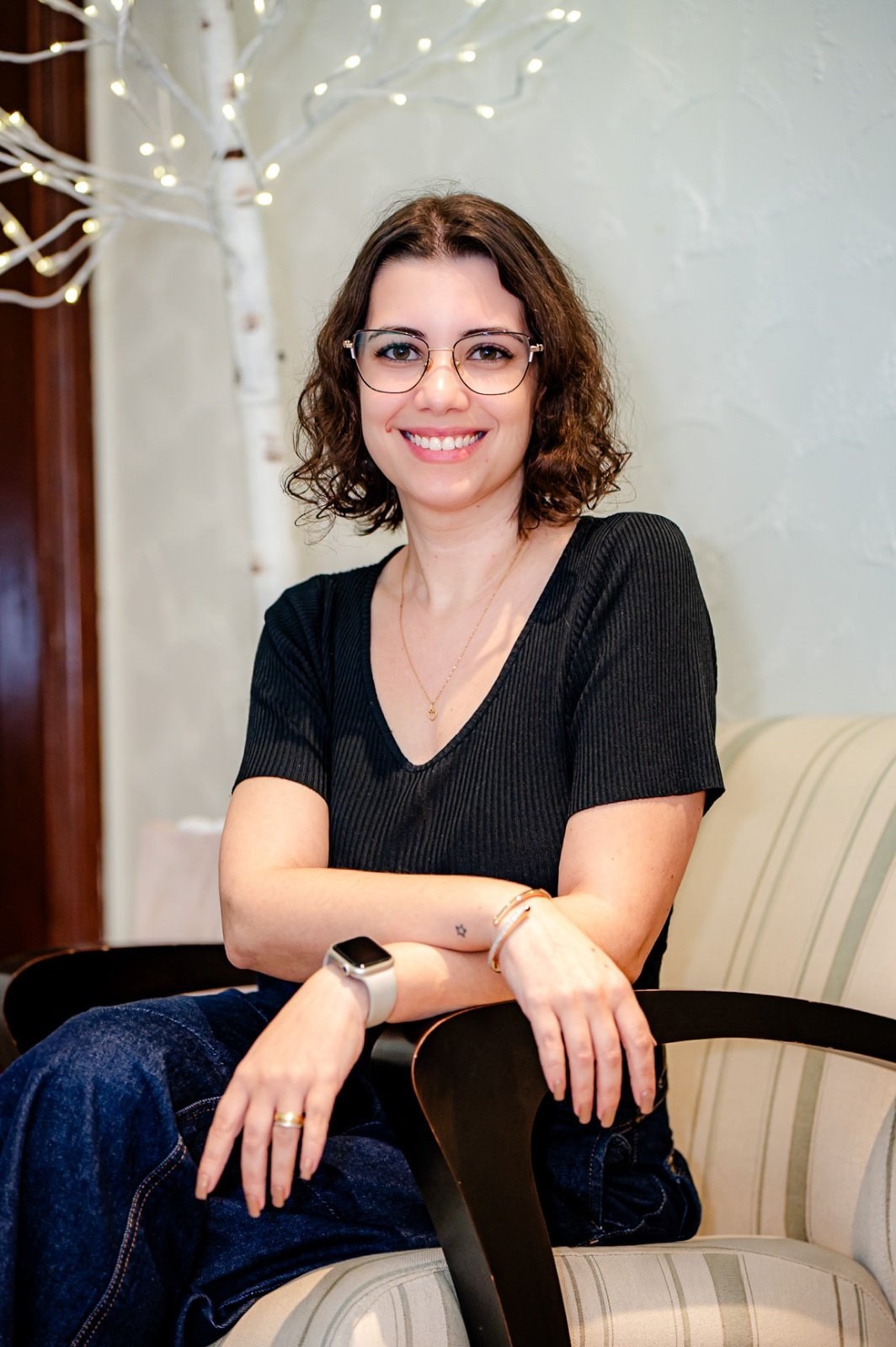 Lorena Mariano sentada em uma poltrona, de braços cruzados sobre o encosto, sorrindo.